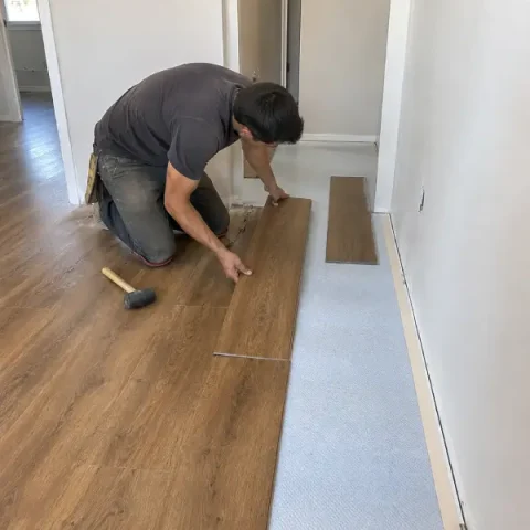 Installer laying new flooring planks in a residential room during installation.