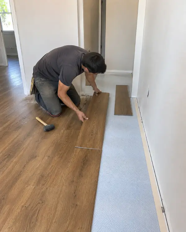 Installer laying new flooring planks in a residential room during installation.